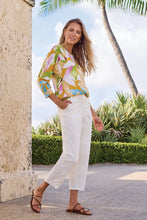 Load image into Gallery viewer, Woman in a colorful floral lightweight sweater and white pants standing outdoors with palm trees in the background.
