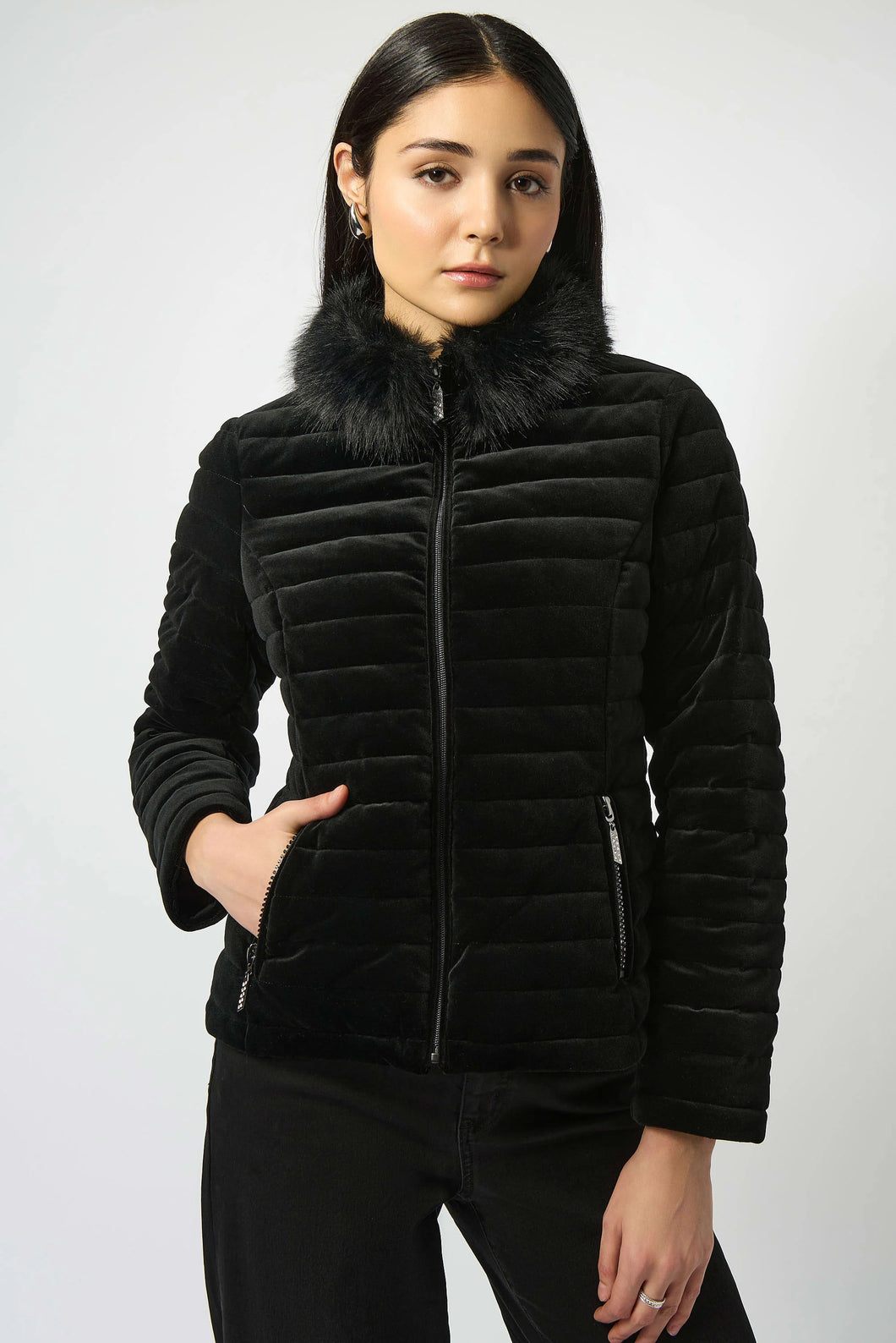 Woman modeling a black quilted jacket with fur collar and black pants against a white background.