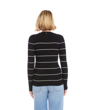 Load image into Gallery viewer, Woman wearing a black sweater with white stripes and light blue jeans against a white wall.
