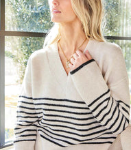 Load image into Gallery viewer, Woman wearing an ecru sweater with black stripes sitting indoors with large windows in the background.
