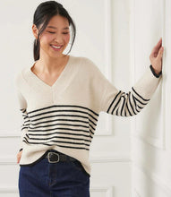 Load image into Gallery viewer, Woman wearing an ecru sweater with black stripes and jeans and belt against a white wall.
