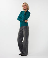 Load image into Gallery viewer, Woman wearing gold a teal turtleneck sweater with gold heart cufflinks, lack jeans and black shoes against a white background.
