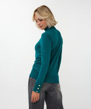 Load image into Gallery viewer, Woman wearing a teal turtleneck sweater with heart cufflinks and black pants against a white background.
