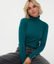 Load image into Gallery viewer, Woman wearing gold earrings, a teal turtleneck sweater with gold heart cufflinks and black jeans against a white background.
