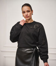 Load image into Gallery viewer, Woman wearing a black sweater with embellished black decorative elements and black skirt against a white background.
