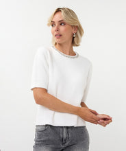 Load image into Gallery viewer, Woman wearing an off-white top with a rhinestone neckline, silver earrings and grey pants against a white background.
