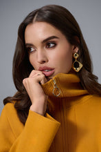 Load image into Gallery viewer, Woman wearing a mustard yellow top and gold earrings against a gray background.
