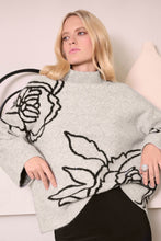 Load image into Gallery viewer, Woman wearing a boxy sweater in light grey with a black floral design and black skirt, standing in a beige room.
