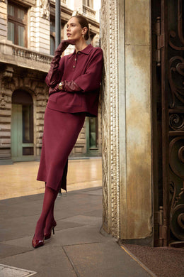 Woman in a burgundy outfit standing against an ornate building entrance.