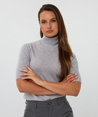 Woman wearing a grey short sleeve turtleneck sweater and grey pants against a white background.