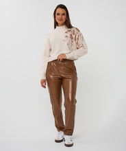 Load image into Gallery viewer, Woman wearing a cream sweater with rose gold floral sequin details, brown leather pants and sneakers against a plain background.

