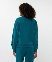 Load image into Gallery viewer, Model wearing a teal outfit with decorative sleeves against a white background.
