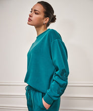 Load image into Gallery viewer, Woman wearing a teal modal sweater with floral embroidery and teal pants against a white wall background.
