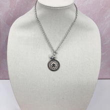 Load image into Gallery viewer, This necklace showcases a stunning and very rare silver vintage quilted button, embellished with a black CC logo. The exquisite button sits in a circular silver setting, encircled by brilliant clear rhinestones, and is suspended from a 925-sterling silver link chain that fastens with a toggle closure. Its unique allure is bound to garner an array of compliments.
