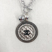 Load image into Gallery viewer, This necklace showcases a stunning and very rare silver vintage quilted button, embellished with a black CC logo. The exquisite button sits in a circular silver setting, encircled by brilliant clear rhinestones, and is suspended from a 925-sterling silver link chain that fastens with a toggle closure. Its unique allure is bound to garner an array of compliments.
