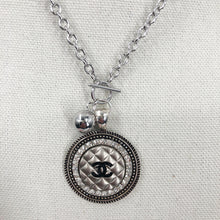 Load image into Gallery viewer, This necklace showcases a stunning and very rare silver vintage quilted button, embellished with a black CC logo. The exquisite button sits in a circular silver setting, encircled by brilliant clear rhinestones, and is suspended from a 925-sterling silver link chain that fastens with a toggle closure. Its unique allure is bound to garner an array of compliments.
