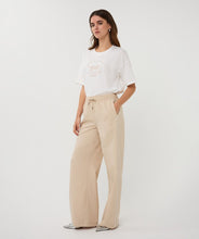 Load image into Gallery viewer, Woman wearing an off-white t-shirt with animal print and tan pants against a white background.
