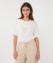 Load image into Gallery viewer, Woman wearing an off-white t-shirt with animal print and tan pants against a white background.

