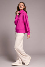 Load image into Gallery viewer, Woman wearing a bright pink funnel neck knit top, white pants and white sneakers against a plain background.
