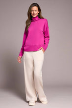 Load image into Gallery viewer, Woman wearing a bright pink funnel neck knit top, white pants and white sneakers against a plain background.
