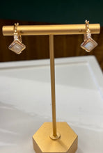 Load image into Gallery viewer, A pair of gold-tone dangle earrings with square moonstones, displayed on a gold jewelry stand.
