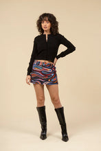 Load image into Gallery viewer, Woman wearing a black sweater, tall black boots and mini skort in abstract pattern against a white background.
