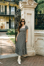 Load image into Gallery viewer, Woman in a brown and white polka dot dress, sunglasses and tall white boots standing next to a stone column in an elegant outdoor setting.

