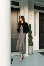 Load image into Gallery viewer, Woman wearing a long checkered dress, black cardigan and black sandals standing in front of a house with a wreath on the door.
