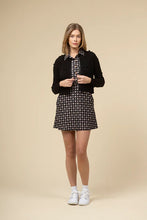 Load image into Gallery viewer, Woman wearing a black cardigan, checkered dress, and white sneakers against a beige background.
