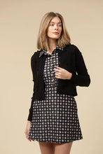 Load image into Gallery viewer, Woman wearing a black cardigan over a patterned dress against a beige background.
