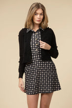 Load image into Gallery viewer, Woman wearing a black cardigan over a patterned dress against a beige background.
