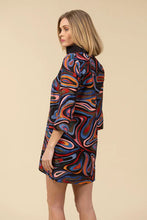 Load image into Gallery viewer, Woman wearing a colorful abstract patterned dress against a light beige background.
