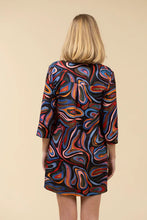 Load image into Gallery viewer, Woman wearing a colorful abstract patterned dress against a light beige background.
