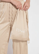 Load image into Gallery viewer, Designed with the modern traveler in mind, the Packable Pleated Palazzo Pant by Lysse blends effortless elegance with functional versatility. Made from silky Soft Touch Satin, these wide-leg trousers feature permanent pleats, an adjustable drawstring waist, and functional side pockets for a flattering yet practical silhouette. The raw-cut hem allows for easy alterations, while the 28-inch inseam makes them ideal for showcasing your favorite sandals or heels.
