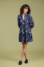 Load image into Gallery viewer, Woman wearing a blue and navy floral dress and black loafers against a pale green background.
