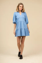 Load image into Gallery viewer, Woman wearing a blue dress with puff sleeves against a beige background.
