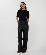 Load image into Gallery viewer, Woman wearing black leather pants and a black short sleeve top against a white background.
