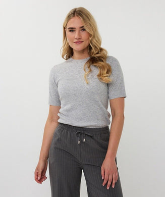 Woman wearing short sleeve grey sparkly top with gray pinstripe pants against a light gray background.