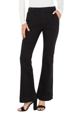 Model wearing long sleeve white top, black denim flare trousers and black heels against a white background.