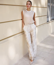 Load image into Gallery viewer, Woman in a beige sleeveless top and white and beige safari pants standing against a light-colored wall.

