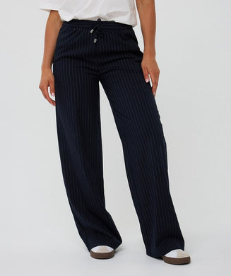Navy pinstripe pants, white top and white sneakers worn by a model against a white background.