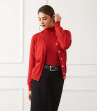 Load image into Gallery viewer, Woman wearing a red cardigan over a coordinating turtleneck, black skirt and black belt  against a white wall.
