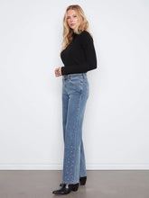 Load image into Gallery viewer, A woman stands in profile wearing a black ribbed long-sleeve top, light blue high-waisted flare jeans with silver rhinestone embellishments down the front of the legs, and black pointed-toe heeled boots against a white wall and gray floor.
