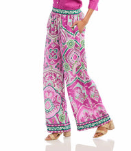 Load image into Gallery viewer, The Wyndy Wide Leg Pants in Pink and Green Multicolor Print by Karen Kane are stylish wide-leg pants featuring a striking Italian tile border print on smooth crepe fabric. They are fitted at the waist and relaxed at the hips, offering a comfortable drape with a pull-on elastic waistband and functional side pockets. Ideal for pairing with solid tops or matching prints, these wide-leg pants can be dressed up with heels or kept casual with sandals.
