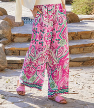 Load image into Gallery viewer, The Wyndy Wide Leg Pants in Pink and Green Multicolor Print by Karen Kane are stylish wide-leg pants featuring a striking Italian tile border print on smooth crepe fabric. They are fitted at the waist and relaxed at the hips, offering a comfortable drape with a pull-on elastic waistband and functional side pockets. Ideal for pairing with solid tops or matching prints, these wide-leg pants can be dressed up with heels or kept casual with sandals.
