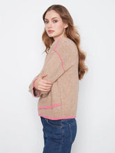 Load image into Gallery viewer, A woman wearing a beige knit sweater with bright pink contrast trim, paired with blue jeans, photographed sideways against a plain white studio background.
