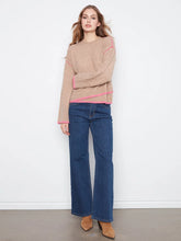 Load image into Gallery viewer, A woman modeling a beige knit sweater with bright pink contrast stitching and blue wide-leg jeans against a white wall.
