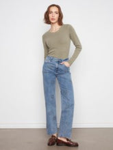 Load image into Gallery viewer, A woman modeling a fitted long-sleeve olive green top and light-wash blue straight-leg jeans, standing against a plain light gray wall.
