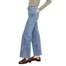 Load image into Gallery viewer, A model wearing light blue wide-leg jeans with stud floral embroidery, paired with a beige long-sleeve top and brown loafers, shown against a plain white background.

