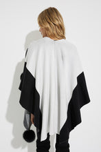 Load image into Gallery viewer, Striking and elegant, our Joseph Ribkoff poncho is the perfect cool weather wardrobe piece.  The gorgeous two-tone fabrication and faux fur pom pom details create a look that is uniquely beautiful and chic. Simply slide one side through the faux fur loop to easily hold the poncho in place and create a chic look. You will certainly make a dramatic entrance when you wear our cozy Tamara poncho. Color- Black and vanilla. Wrap around poncho. Faux fur pom poms and faux fur loop. No pockets.
